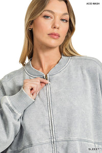 A woman wearing a light gray acid wash zip-up sweatshirt with ribbed collar and cuffs, featuring a drawstring at the neckline.