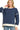 A woman wearing a navy blue crewneck sweatshirt with cream-colored trim on the sleeves, neckline, and hem, paired with light blue jeans.