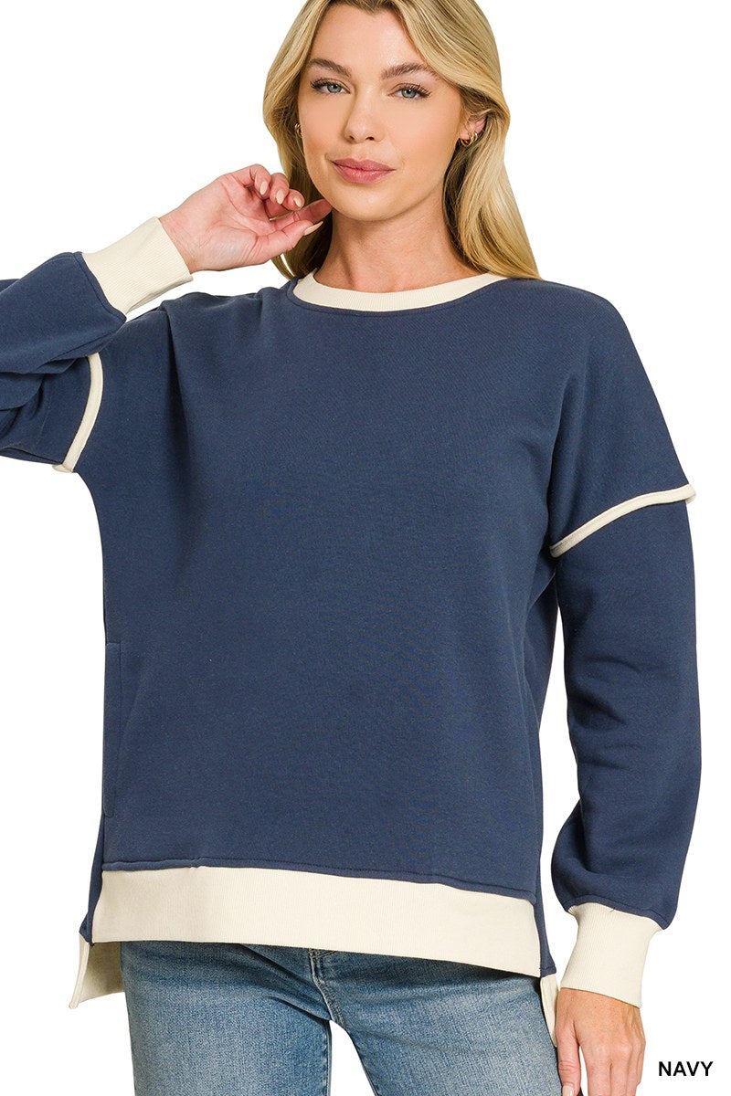 A woman wearing a navy blue crewneck sweatshirt with cream-colored trim on the sleeves, neckline, and hem, paired with light blue jeans.
