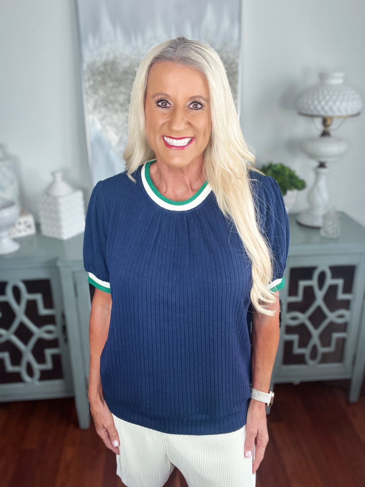 Woman wearing a navy ribbed knit short-sleeve top with white and green trim at the neckline and cuffs, paired with white ribbed pants.