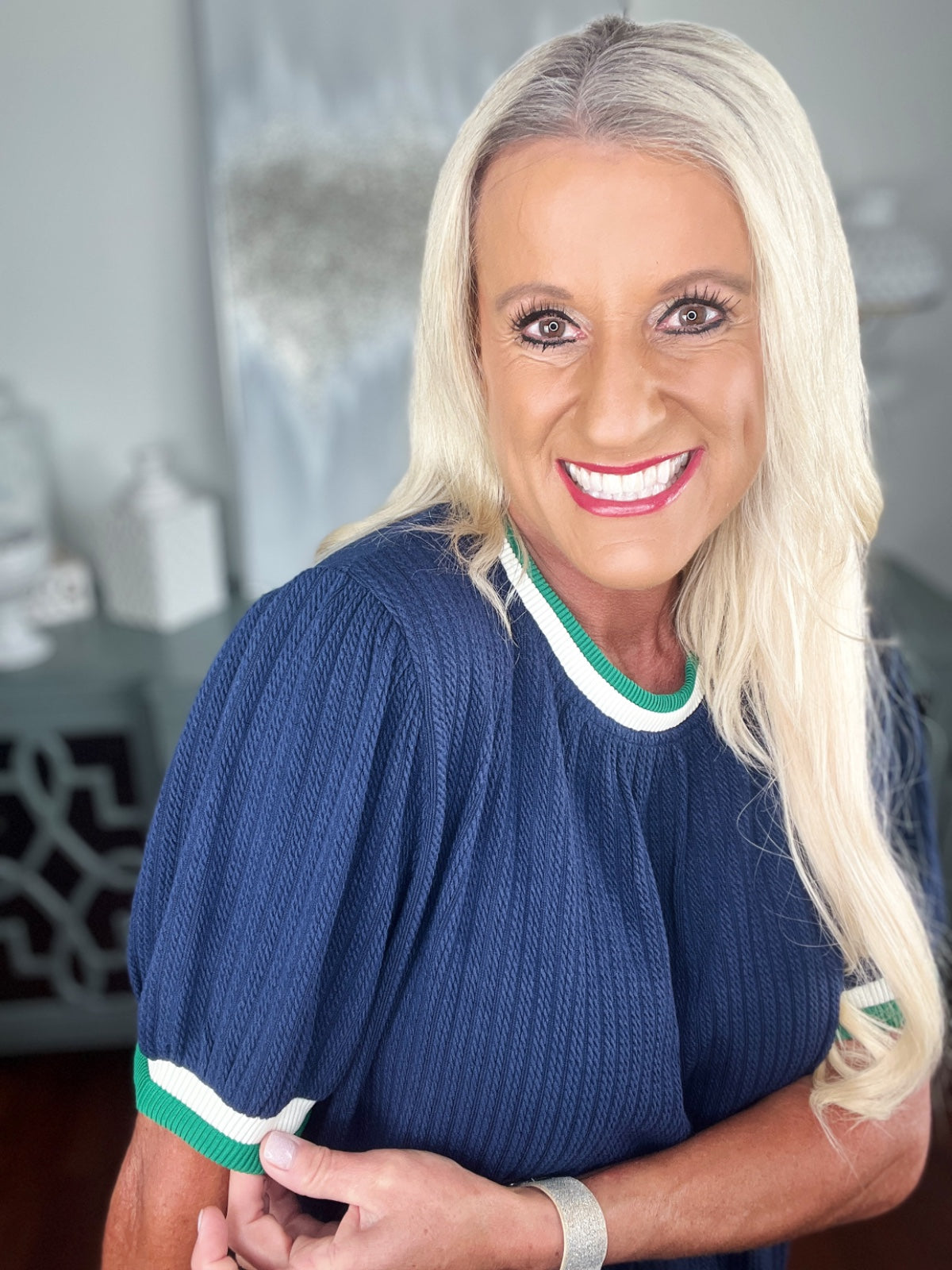 A woman wearing a navy blue ribbed knit sweater with white and green striped trim at the neckline and short sleeves, paired with a silver bracelet.