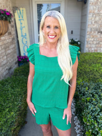 Woman wearing a vibrant green textured two-piece set consisting of a short-sleeve top with ruffled cap sleeves and matching shorts, styled for a casual, modern look.