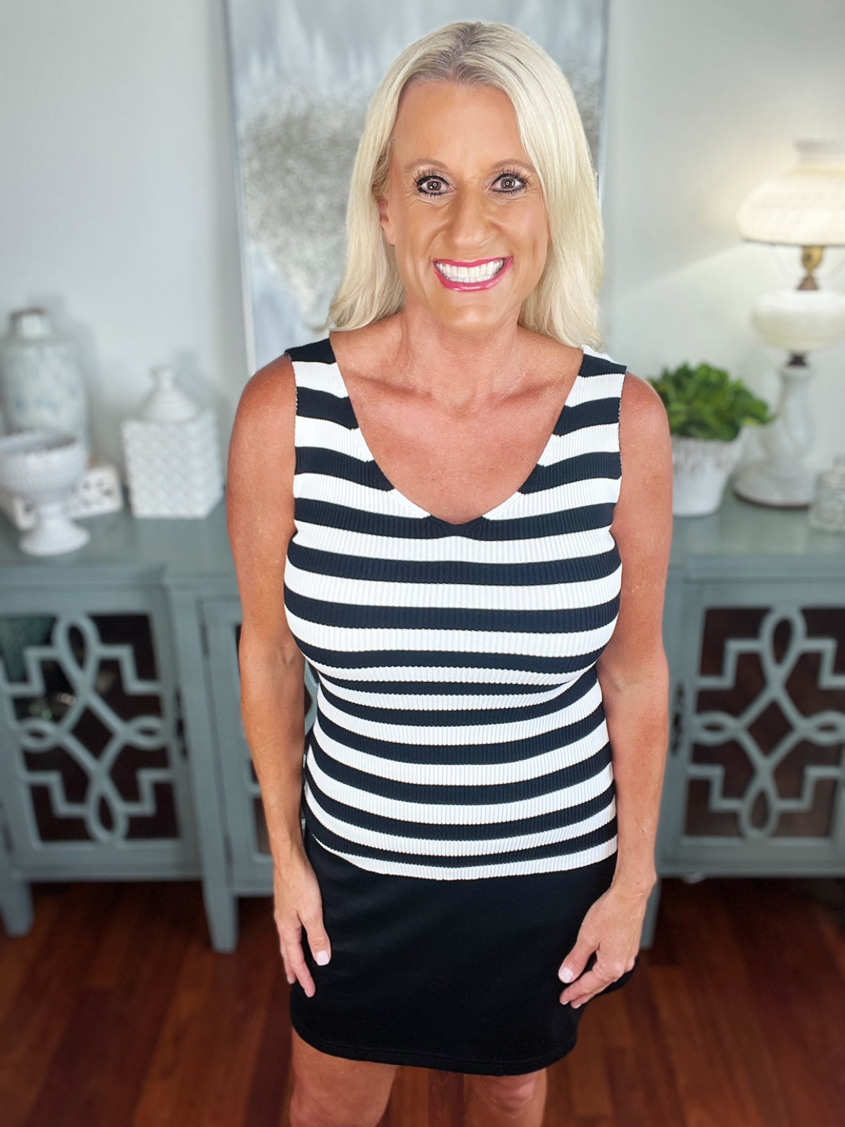 Woman wearing a sleeveless V-neck tank top with black and white horizontal stripes paired with a black skirt, styled in a bright, modern interior setting.