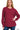 A woman wearing a cabernet-colored knit sweater with a textured pattern, long sleeves with ribbed cuffs, and a ribbed hem, paired with blue jeans.
