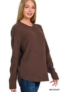 A woman wearing a mahogany brown textured knit sweater with long sleeves and ribbed cuffs, styled over dark blue jeans against a white background.