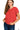 A woman wearing a ruby red short-sleeved knit sweater with a textured waffle knit pattern, paired with dark blue jeans. The sweater features a classic crew neckline and relaxed fit.