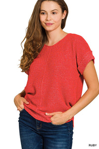 A woman wearing a ruby red short-sleeved knit sweater with a textured waffle knit pattern, paired with dark blue jeans. The sweater features a classic crew neckline and relaxed fit.