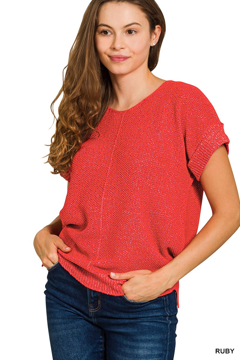A woman wearing a ruby red short-sleeved knit sweater with a textured waffle knit pattern, paired with dark blue jeans. The sweater features a classic crew neckline and relaxed fit.