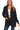 A woman wearing a black waffle-knit cardigan with front pockets over a white ribbed crop top and dark blue jeans. The cardigan features a relaxed fit with long sleeves and ribbed cuffs and hem.