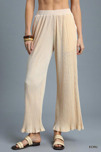 A woman wearing cream-colored pleated wide-leg pants with a relaxed fit and cropped ankle length, paired with black and tan strappy sandals.