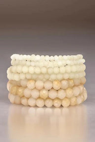 Stack of beige beaded bracelets on a reflective surface with a neutral background