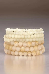 Stack of beige beaded bracelets on a reflective surface with a neutral background