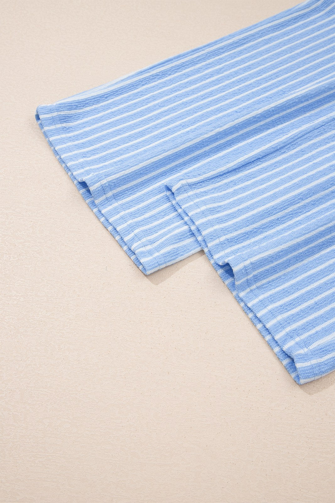 A light blue and white striped fabric laid flat on a neutral background, showing vertical pinstripes and folded edges with visible stitching detail.