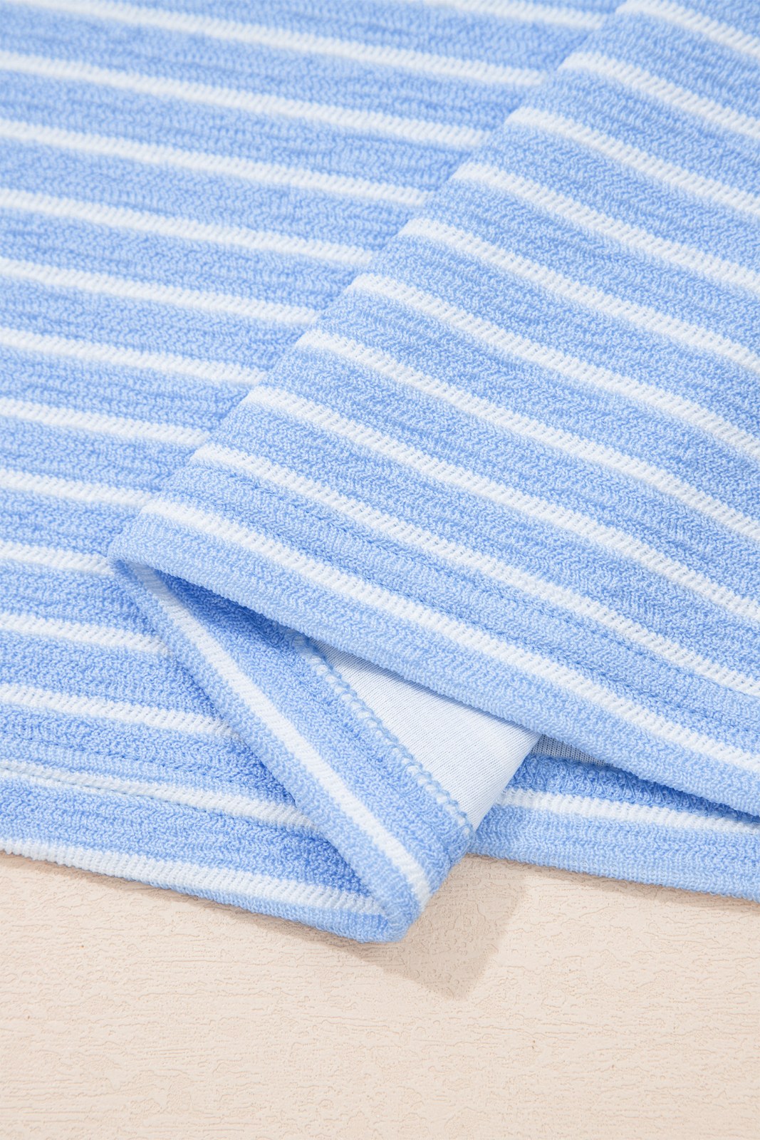 A light blue and white striped towel folded to show its soft, textured surface and finished edge against a neutral background.