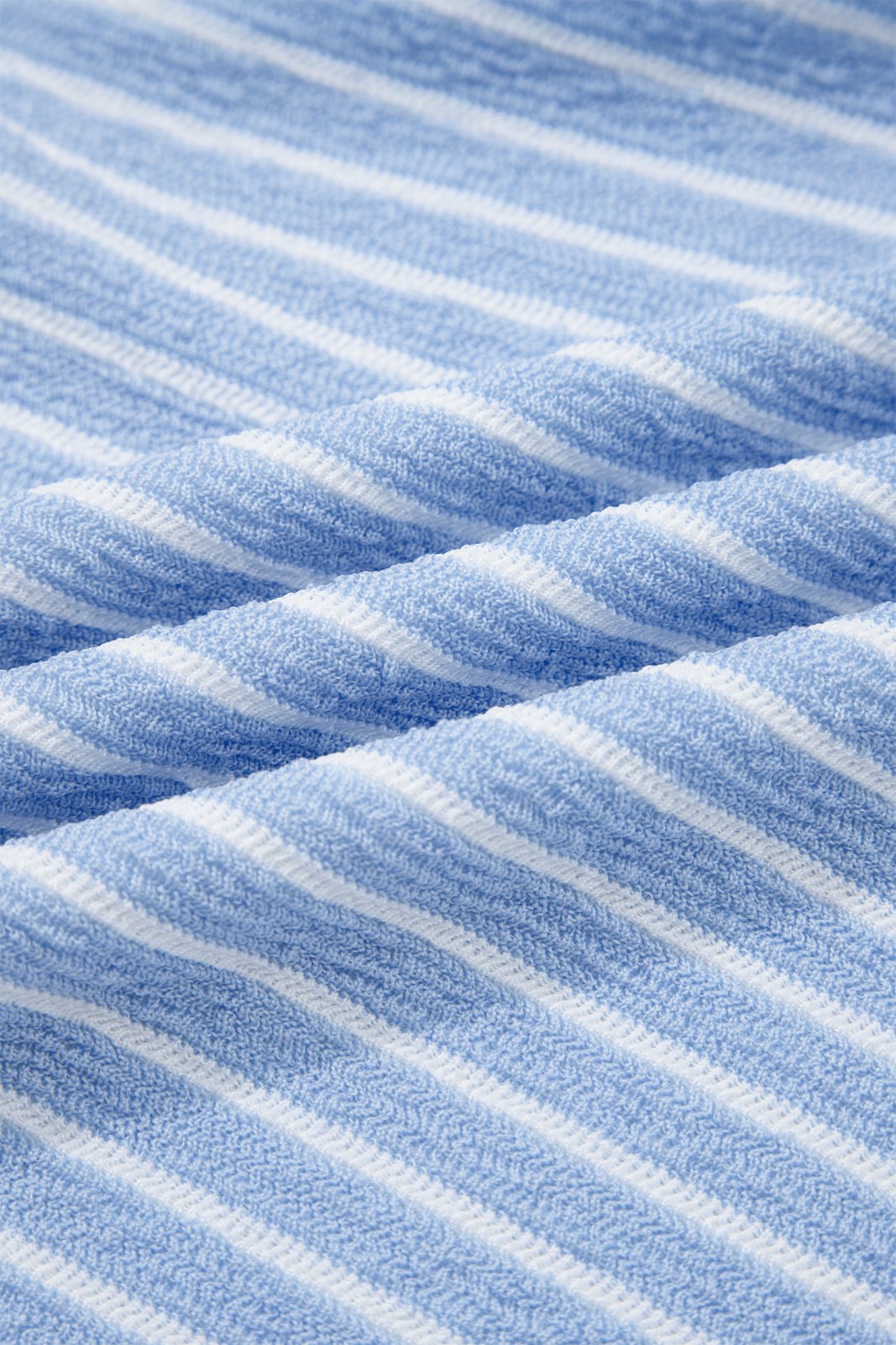 Close-up of a blue and white striped knit fabric showing vertical ribbed texture and diagonal folds in the material.