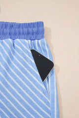 Blue and white striped shorts with an elastic waistband and a black item partially visible in the front pocket, displayed flat against a beige background.