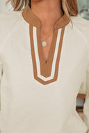 A cream-colored waffle knit top featuring a brown and white geometric patterned collar with a V-neckline, paired with a delicate silver pendant necklace.