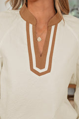 A cream-colored waffle knit top featuring a brown and white geometric patterned collar with a V-neckline, paired with a delicate silver pendant necklace.