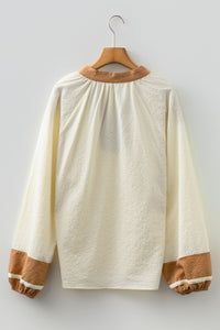 A cream-colored long-sleeve sweatshirt with a textured quilted fabric, featuring a tan ribbed crew neckline and matching tan ribbed cuffs on the sleeves, displayed on a wooden hanger against a white background.