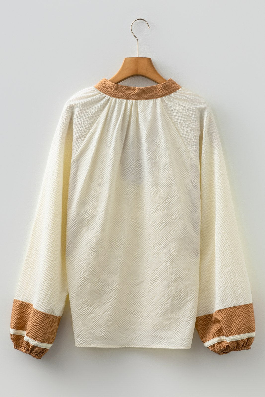 A cream-colored long-sleeve sweatshirt with a textured quilted fabric, featuring a tan ribbed crew neckline and matching tan ribbed cuffs on the sleeves, displayed on a wooden hanger against a white background.