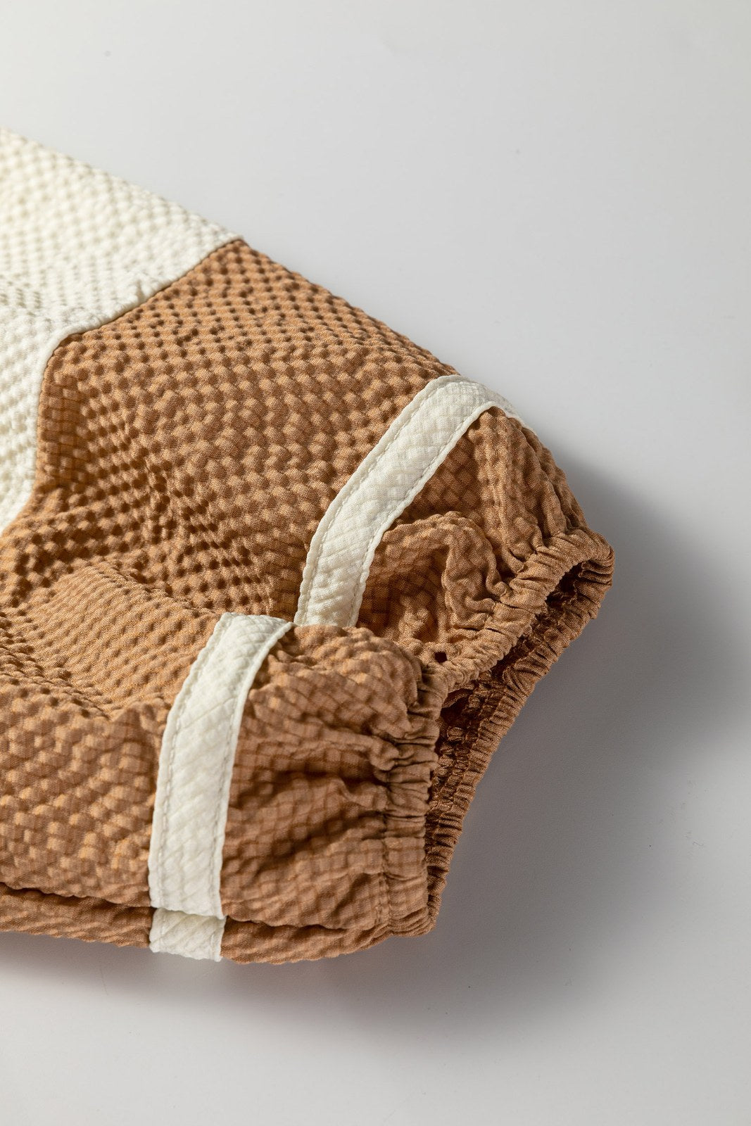 Close-up of a two-tone waffle-knit garment featuring caramel brown and cream colored sections with white elastic trim at the cuffs and neckline.