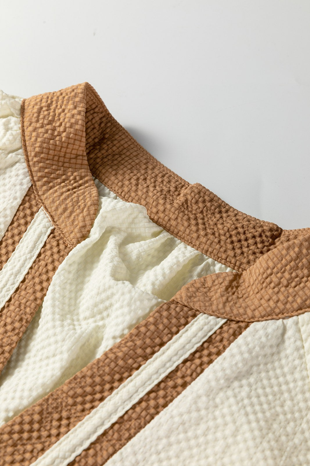 A close-up view of a quilted garment featuring alternating stripes of warm tan and cream textured fabric with visible stitching details and soft gathering along the seams.