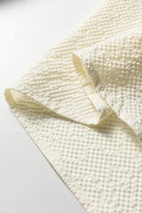 Close-up detail of a cream-colored knit sweater showing textured waffle weave fabric with ribbed trim and finished seams on the sleeve edge.