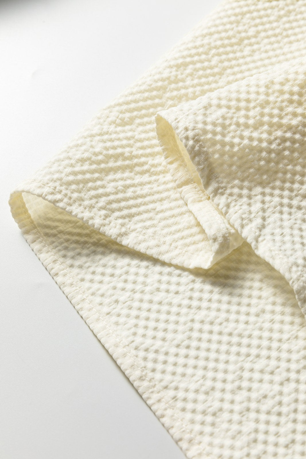 Close-up detail of a cream-colored knit sweater showing textured waffle weave fabric with ribbed trim and finished seams on the sleeve edge.