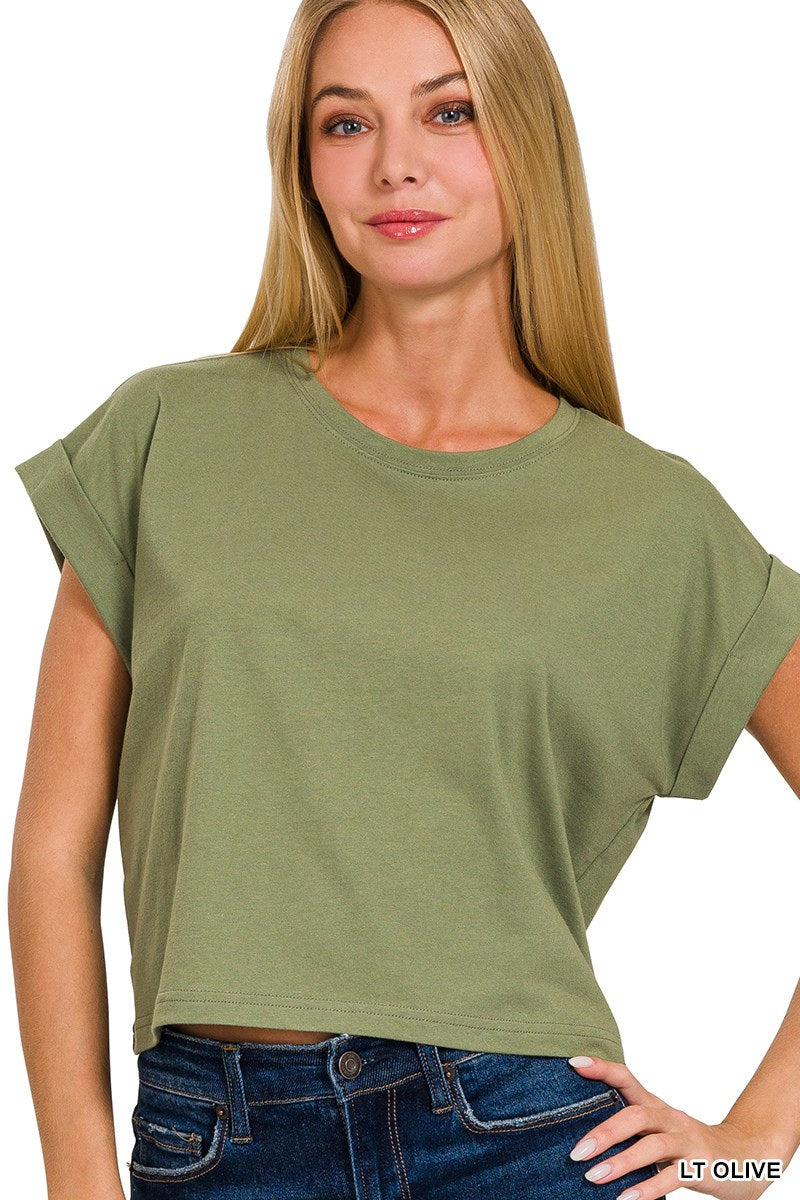 A woman wearing a light olive green short-sleeved crop top with a relaxed fit and rolled cuffs, paired with dark blue jeans.