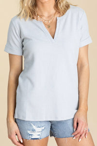 Woman wearing a light gray ribbed top and denim shorts on a beige background